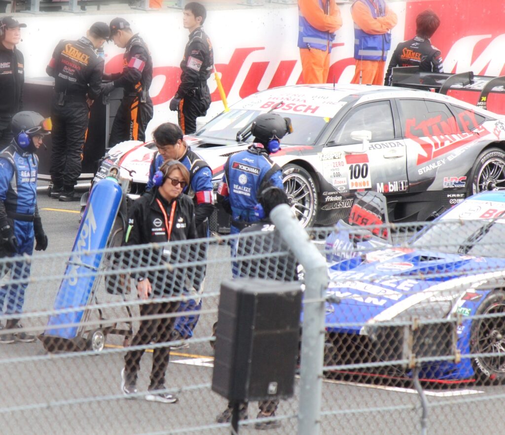 SUPER GTもてぎ2025のピットロードでファンサービスをする近藤真彦監督。KONDO Racingの監督として登場し、観客の声援に応える様子。