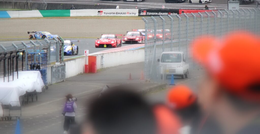 SUPER GTもてぎ2025の決勝戦を応援スタンドから撮影。観客席越しにコーナーへ突入するGT500・GT300マシンの迫力をとらえた写真。